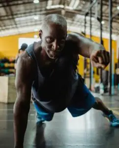middle age man fist bumping while doing planks - try strength training over 50