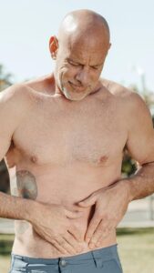 Shirtless middle age man holding stomach - bone broth for a happy gut