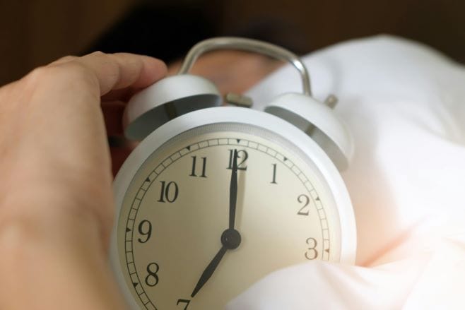 man holding alarm clock in bed